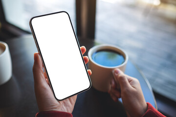 Mockup image of a woman holding mobile phone with blank desktop screen while drinking coffee in cafe