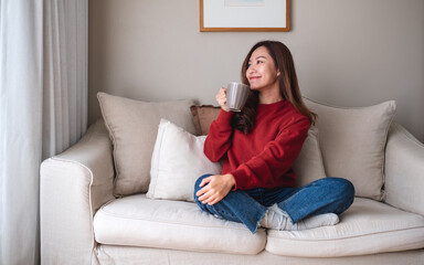 Portrait image of a beautiful asian woman drinking hot coffee and relaxing on a sofa at home