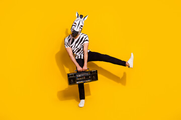 Photo of cheerful funny man wear zebra print t-shirt mask listening boombox dancing isolated yellow...