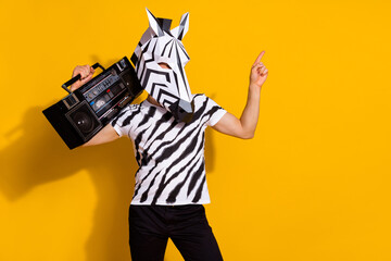 Photo of cool eccentric man wear zebra print t-shirt mask listening boombox pointing empty space isolated yellow color background