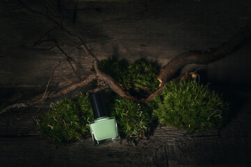 Green nail polish bottle on drak green moss background. Green nail polish bottle lay on live dark...