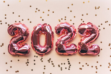 Balloons made of pink foil in the form of numbers 2022 with confetti on a pink background. Celebrating Christmas, New Year and festive concept. Flat lay, top view.
