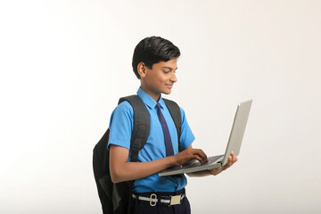 Indian school boy in uniform and using laptop on white background.