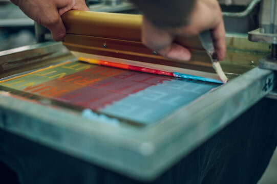 Male worker pressing ink on frame while using the printing machine in a workshop