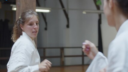 Handheld shot of focused girl fighting with her opponent in gym. Front view of excited martial artsist wearing kimono improving skills, demonstrating basic karate poses. Sport, sparring concept - Powered by Adobe