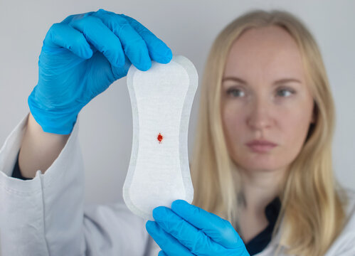Hypomenorrhea. The woman shows a gynecological pad with a small drop of blood on it. Concept of small amounts during scanty menstruation. Complaints of pain and strange cycle. Diseases in gynecology