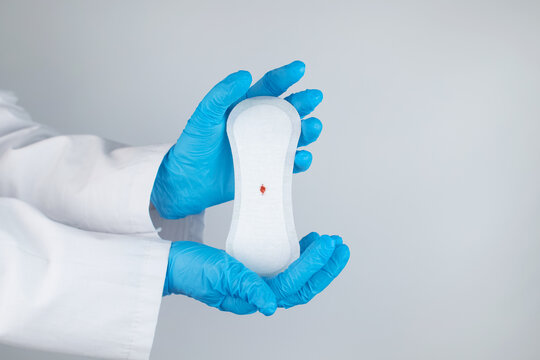 Hypomenorrhea. The woman shows a gynecological pad with a small drop of blood on it. Concept of small amounts during scanty menstruation. Complaints of pain and strange cycle. Diseases in gynecology