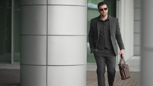 slow motion elegant businessman in suit wear sunglasses holding briefcase walking in the urbanc ity street 