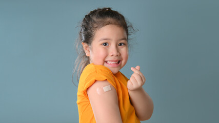 Coronavirus Vaccination Advertisement. Happy Vaccinated Little asian girl Showing Arm With Plaster...
