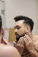 Worried man looking at mirror and checking how dense is his beard after taking shower