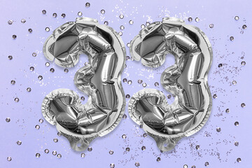 Silver foil balloon number, digit thirty three on a lilac background with sequins. Birthday greeting card with inscription 33. Top view. Numerical digit. Celebration event, template.