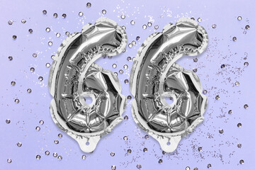 Silver foil balloon number, digit sixty six on a lilac background with sequins. Birthday greeting card with inscription 66. Anniversary concept. Top view. Numerical digit. Celebration event, template.