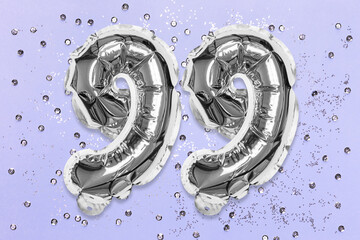 Silver foil balloon number, digit ninety nine on a lilac background with sequins. Birthday greeting card with inscription 99. Top view. Numerical digit. Celebration event, template.