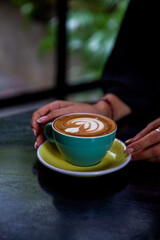 green mug of cappuccino with latte art on wooden background.