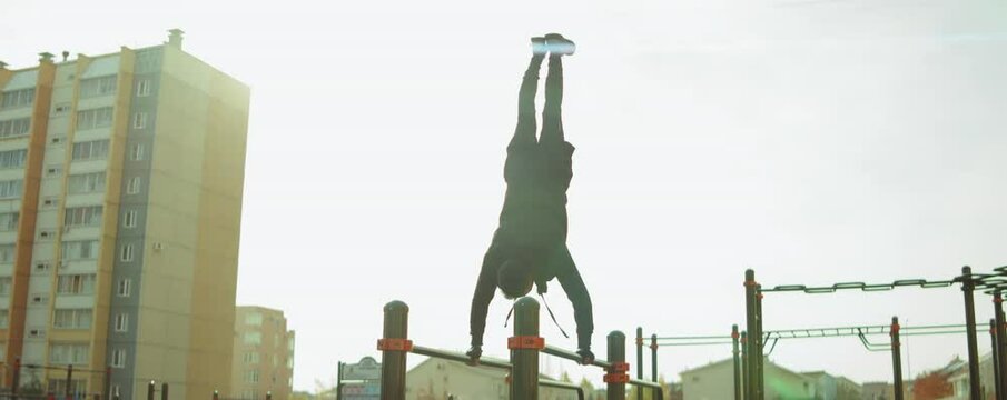 Young sportsman performing handstand on parallel bars while training outdoors on workout playground