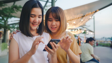 Happy young Asia women tourist with casual style look at photo on smartphone screen on mobile phone with river view sunset near cafe in city town at night. Lifestyle tourist travel holiday concept. © tirachard