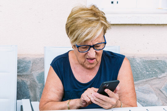 Retired elderly woman consulting the mobile phone in an outdoor space sitting. Grandparents, retirees and technology concept.