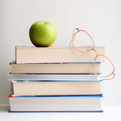 Stack of books on table, on white background. Green apple and glasses.