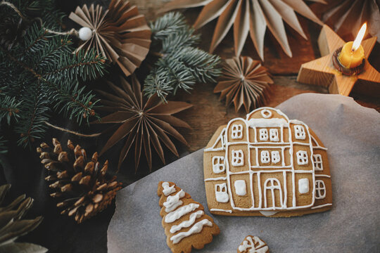 Christmas gingerbread cookies with icing on rustic wooden table with candle and ornaments, flat lay. Making gingerbread house with frosting. Atmospheric moody image. Merry Christmas!