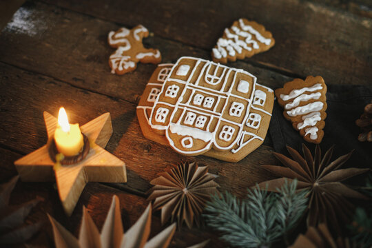 Christmas gingerbread cookies with icing on rustic wooden table with candle and ornaments. Making gingerbread house with frosting. Atmospheric moody image. Merry Christmas and Happy Holidays!