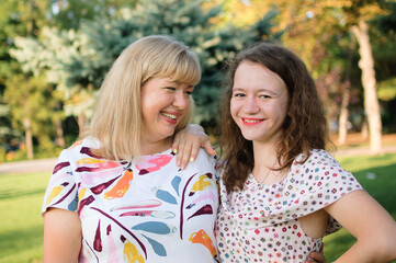 Female portrait of a beautiful plus size blond, blue-eyed mother and daughter in the park during summer. Family day, happy people concept