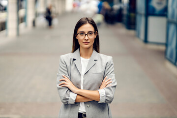 A young serious, elegant businesswoman standing on the street with arms crossed and looking at the...