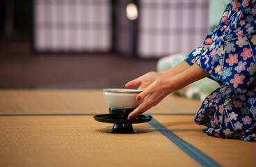 Japanese woman in traditional kimono, kneeling on Seiza position, during the tea ceremony.