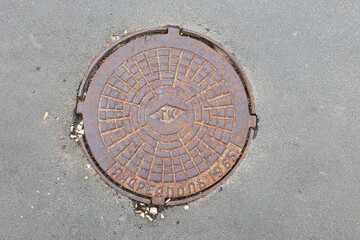 Old iron manhole cover on the city street. Translation: Abbreviation for Urban Canadianization, Andreapol