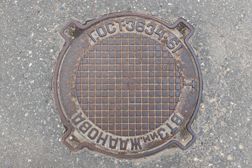 Old iron manhole cover on the city street. Translation: abbreviation for State Standard, Zhdanov...
