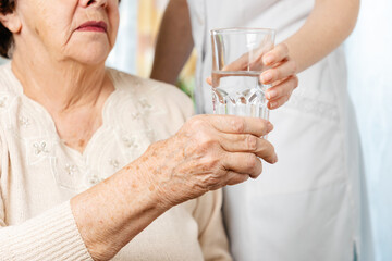 A senior woman takes a glass of water from a nurse. The concept of caring for the older generation