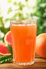 Glass of delicious grapefruit juice on wooden table against blurred background