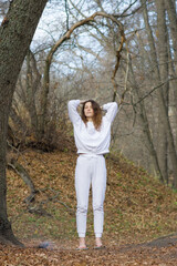 Naklejka premium A woman in white clothes in a relaxed pose stands calmly on nails outdoors in a park. Standing with bare feet on a sadhu board. Relaxation exercises, nail therapy, yoga, meditation. Copy space