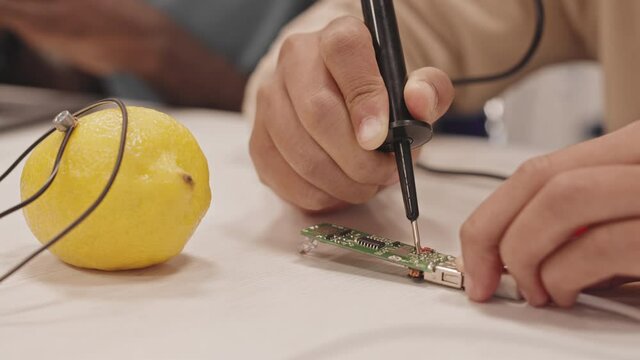 Close-up of child hands soldering microcircuits at table with lemon and wires on in classroom