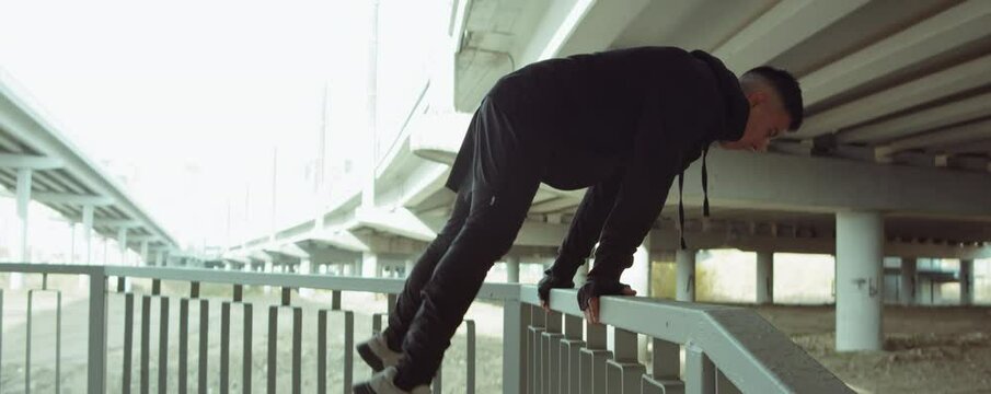 Arc shot of male athlete in sports outfit performing straddle planche on urban railing during street workout in city