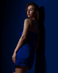 Young and cute brunette woman in blu dress posing on dark blue background free space for text