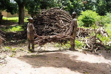 Two little black African brothers piling bunches of wood for charcoal production