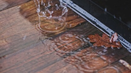 Raindrops Hitting Surface of Water Puddle Accumulated on Terrace Wooden Plank Floor on Rainy Autumn Day Creating Beautiful Splashes