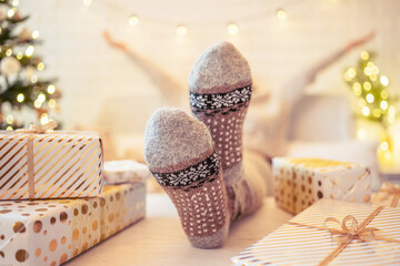 Woman sitting on couch near christmas tree. Female legs, feet in winter woolen socks putting on the...