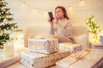 Unfocused, blur woman sitting and relaxation near christmas tree talking on the phone after finishing pakking gift boxes for family.
