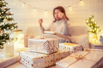 Obraz premium Woman sitting on couch near christmas tree and packing handmade gift boxes putting it on the table. Presents for family.