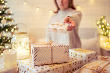 Woman sitting on couch near christmas tree and packing handmade gift boxes putting it on the table. Presents for family.