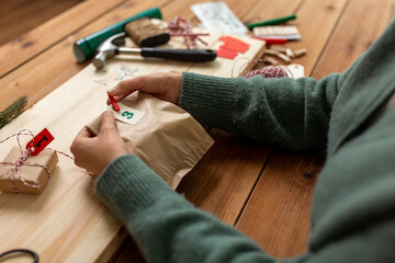winter holidays and hobby concept - hands with clothespin, craft paper bag and tag making advent...