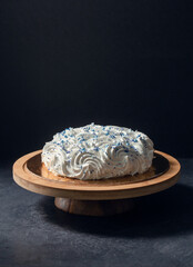 food, sweets and objects concept - meringue or zephyr cake with blue sprinkles on wooden stand over...