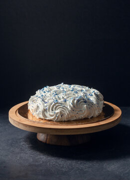 food, sweets and objects concept - meringue or zephyr cake with blue sprinkles on wooden stand over dark background