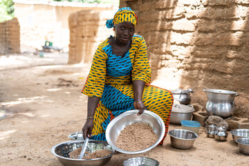 Black African housewife sitting in her open-air kitchen and distributing the food for her family...