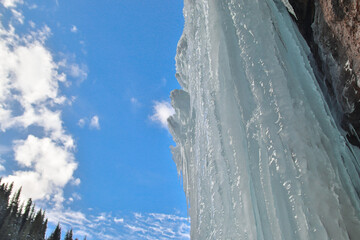 A huge frozen block of ice hangs on a rock, a winter waterfall against a blue sky in Almaty region