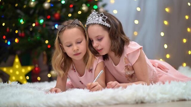 two beautiful and happy little girls in pink dresses at the Christmas tree. the relations of the sisters in the family. Happy New Year. fashionable elegant clothes for girls.