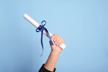 Student holding rolled diploma with ribbon on light blue background, closeup - obrazy, fototapety, plakaty