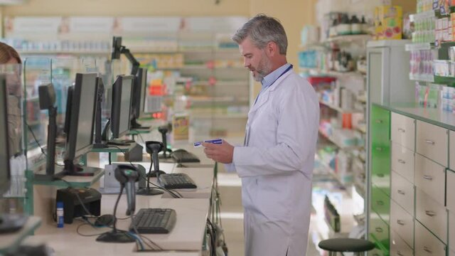 Caucasian doctor in labcoat selling drugs to female customer. Blonde caucasian woman complaining headache flu symptoms to the pharmacist.