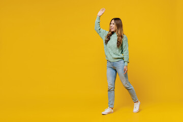 Fototapeta na wymiar Full body young smiling satisfied happy fun woman 30s wearing green knitted sweater walk go strolling waving hand isolated on plain yellow color background studio portrait. People lifestyle concept.